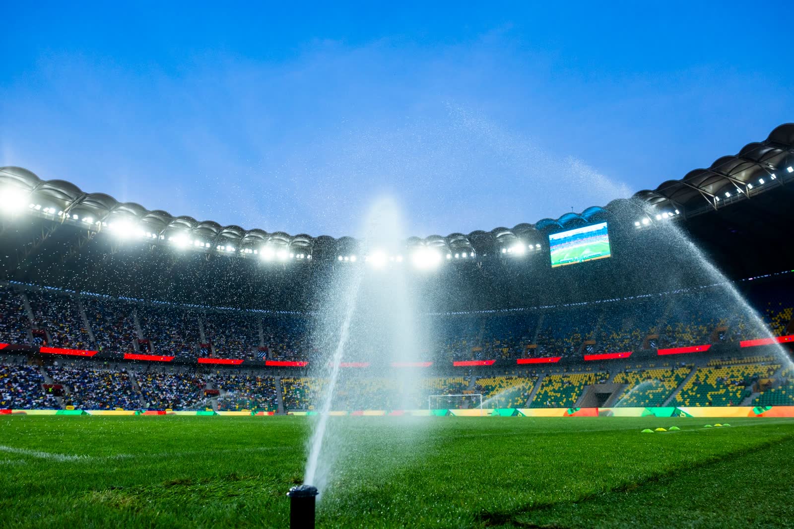Floodlit home field at night with sprinklers running